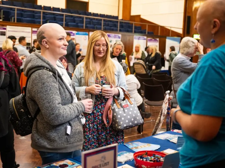 A lively event scene with attendees engaging at tables displaying information and products in a spacious hall.