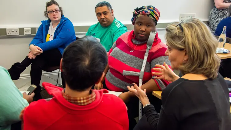 Six people sat in circle listening to speaker.