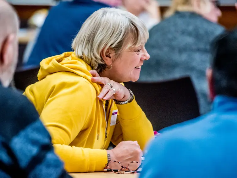 A person leaning over looking at something and smiling in a busy room.